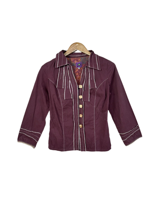 Maroon shirt with white accents on a hanger against a brick wall.