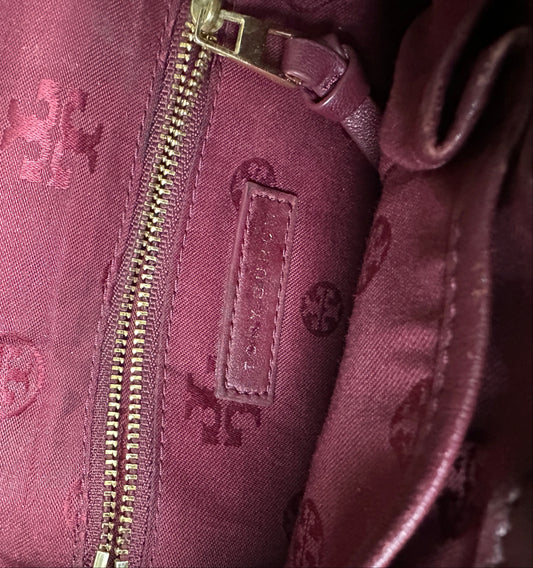 Close-up of a maroon handbag with a gold zipper and brand logo.