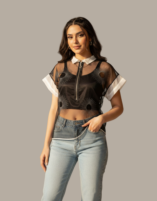 Woman wearing a black sheer top with white accents and light blue jeans on a gray background