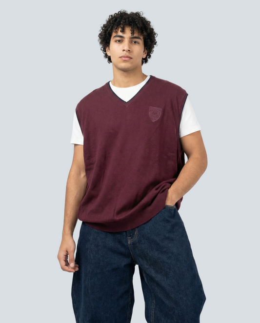 Person wearing a maroon sweater vest over a white shirt with blue jeans on a white background